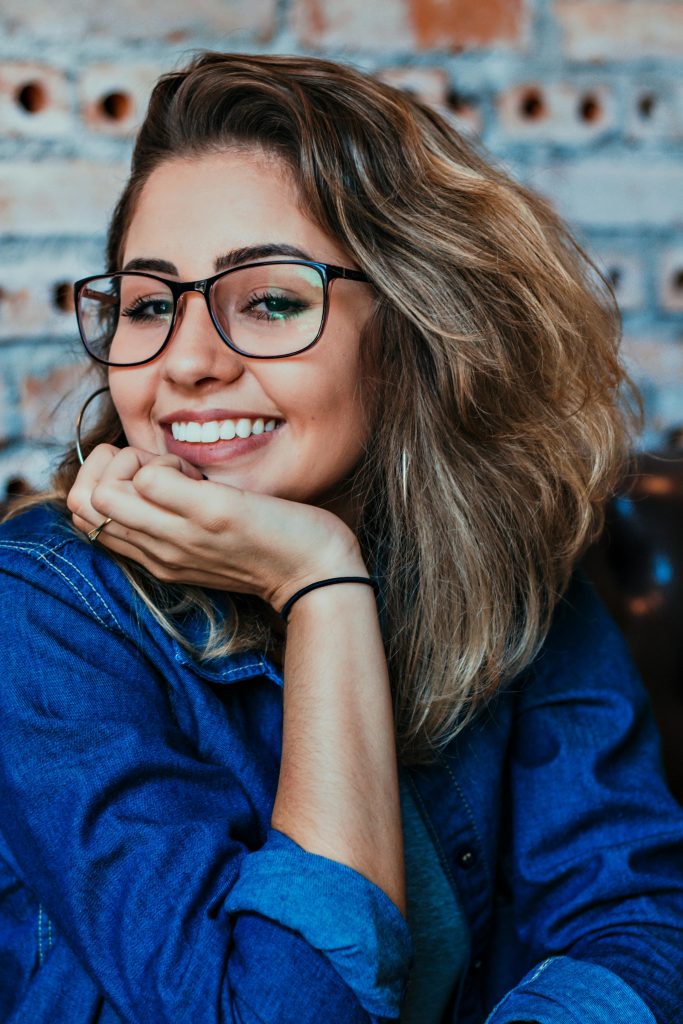 ortodoncia invisible imagen de mujer sonrindo con la mano apoyada en la barbilla, lleva gafas